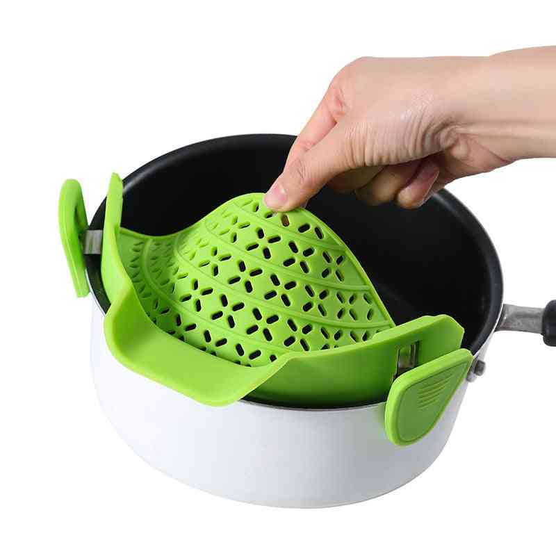 Hand adjusting a green silicone pot side drain clipped onto a saucepan, ensuring a secure fit for spill-proof straining.