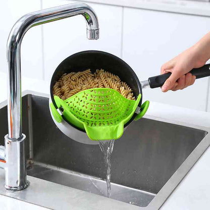 Green silicone pot side drain attached to a saucepan, straining pasta over a sink for easy and mess-free pouring.