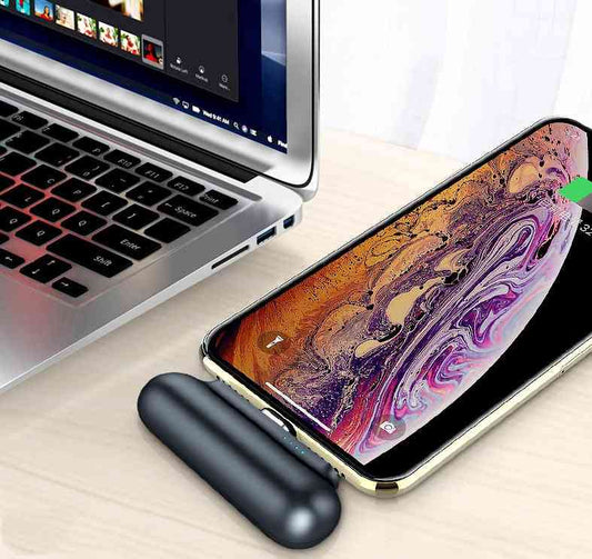 Portable charger connected to an iPhone, charging on a desk beside a laptop. Compact power bank with magnetic connection for easy use.