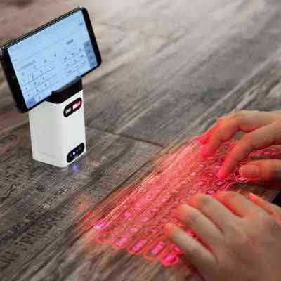 LEING FST Virtual Laser Keyboard Bluetooth Projector projecting a red laser keyboard on a wooden surface while connected to a smartphone.