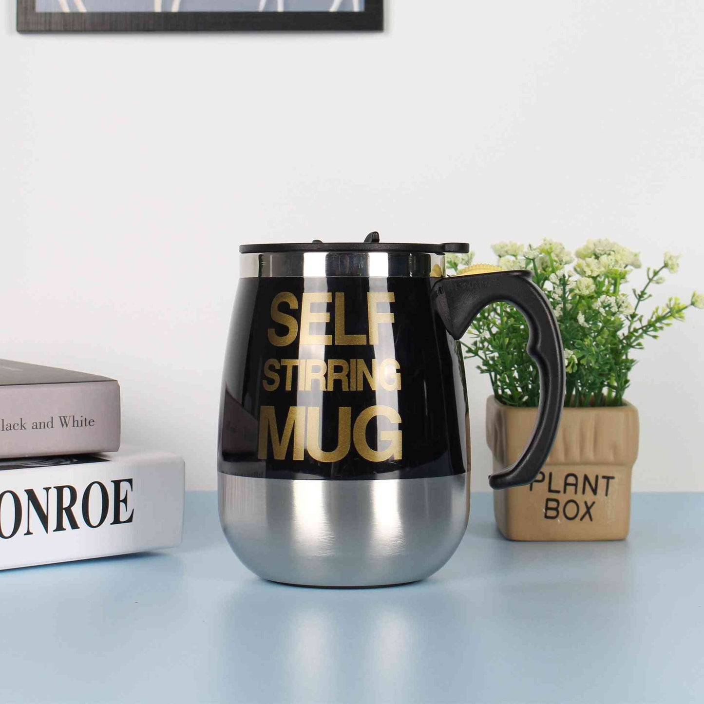 Black self-stirring electric coffee mug with stainless steel base and bold gold lettering, perfect for effortless mixing of beverages.