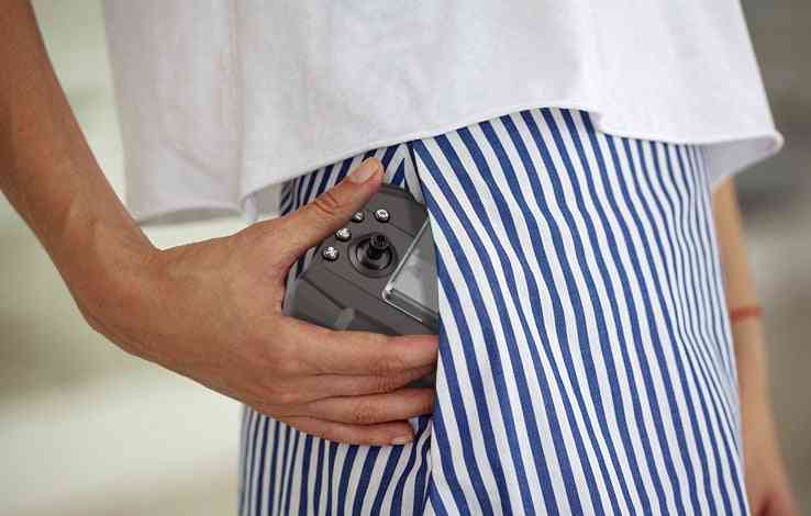 Close-up of mini drone remote control being placed into a pocket, highlighting its compact size.