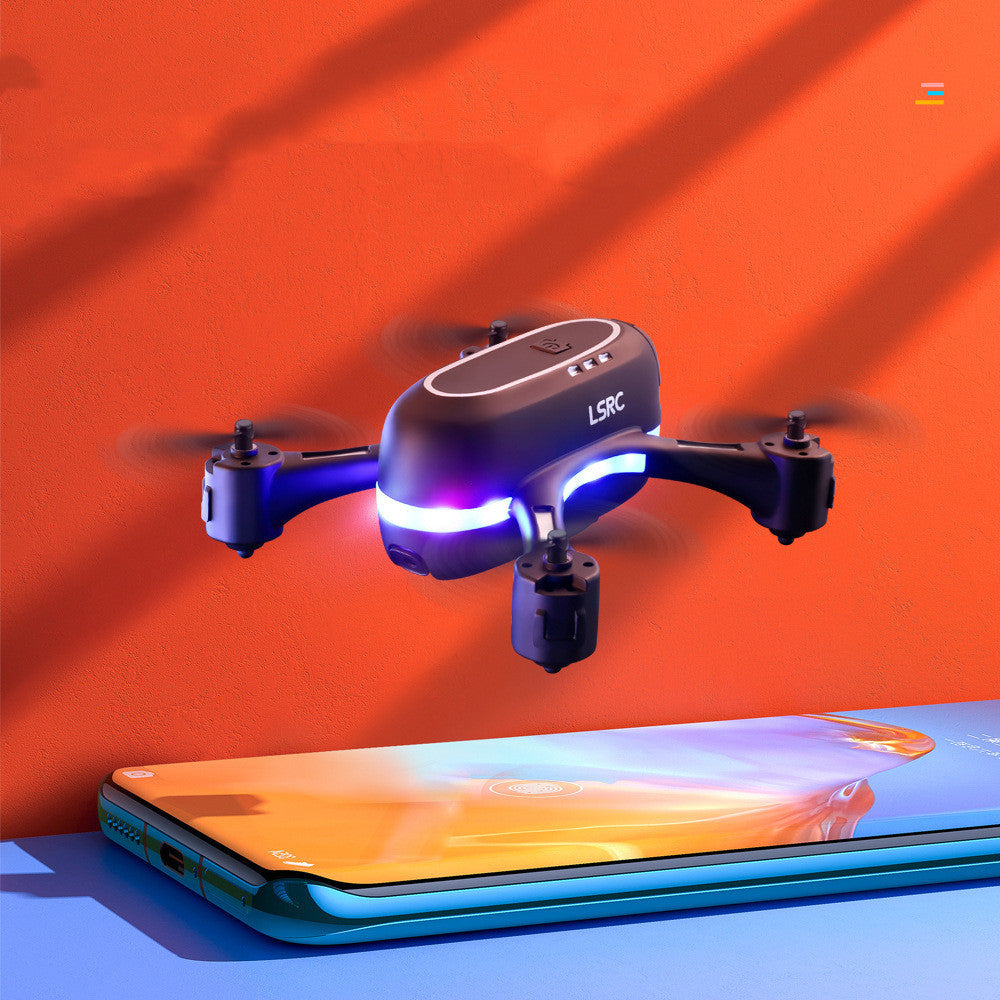 Black mini remote control airplane with LED lights flying above a smartphone against an orange background. Compact and easy-to-fly drone for aerial photography.